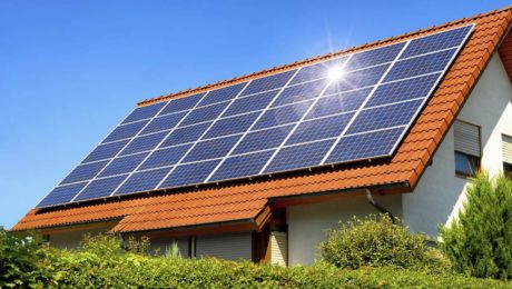Solar panel on a red roof reflecting the sun and the cloudless blue sky